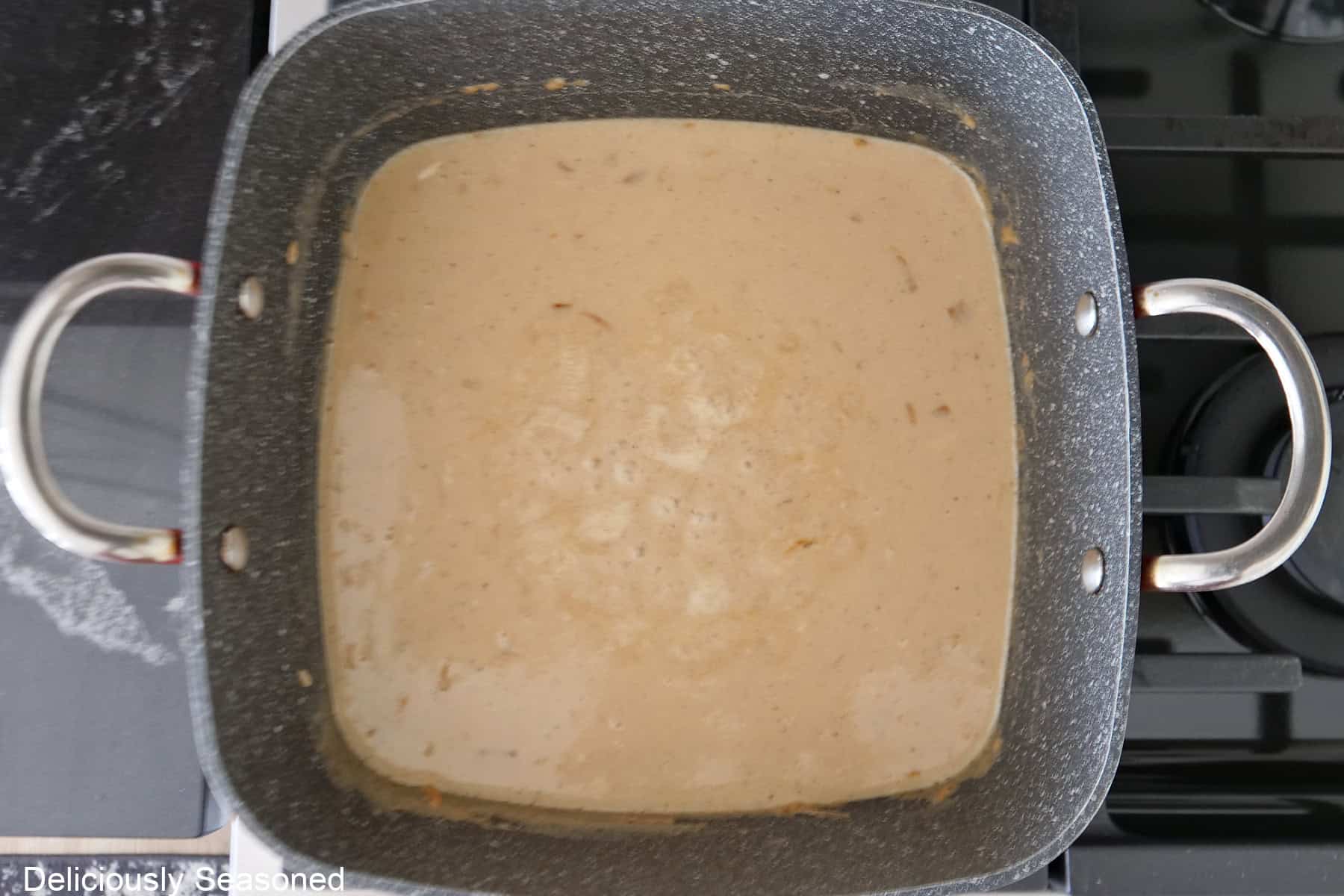 A square pot with the creamy sauce in it on a low boil.