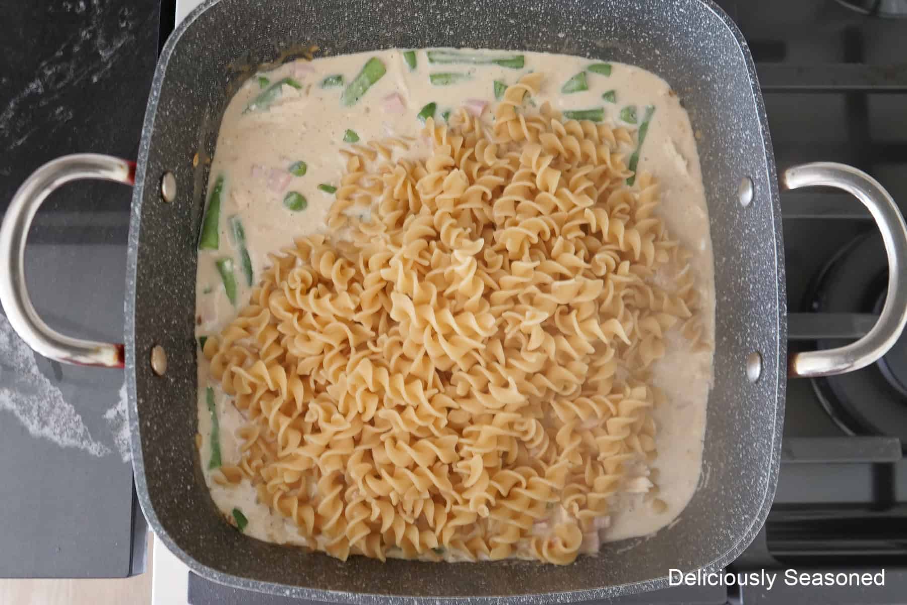 A square pot with the creamy sauce, shredded chicken, green beans, and noodles added to the pot.