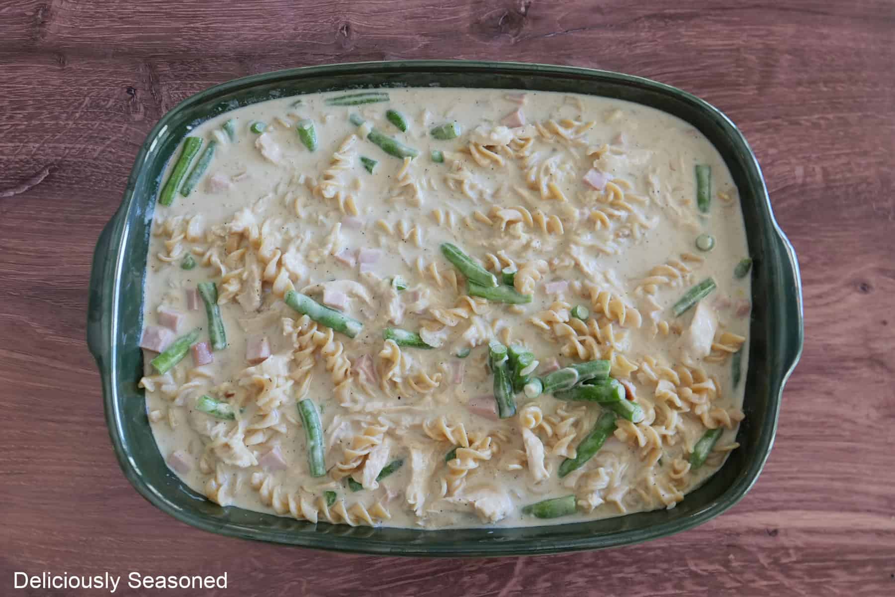 A large green baking dish with the chicken green bean casserole mixture in it before being topped with shredded cheese and crispy fried onions added to the top.