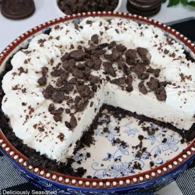 A blue floral pie dish with an Oreo cookie cream cheese pie in it topped with homemade whipped cream and chocolate crunch topping.
