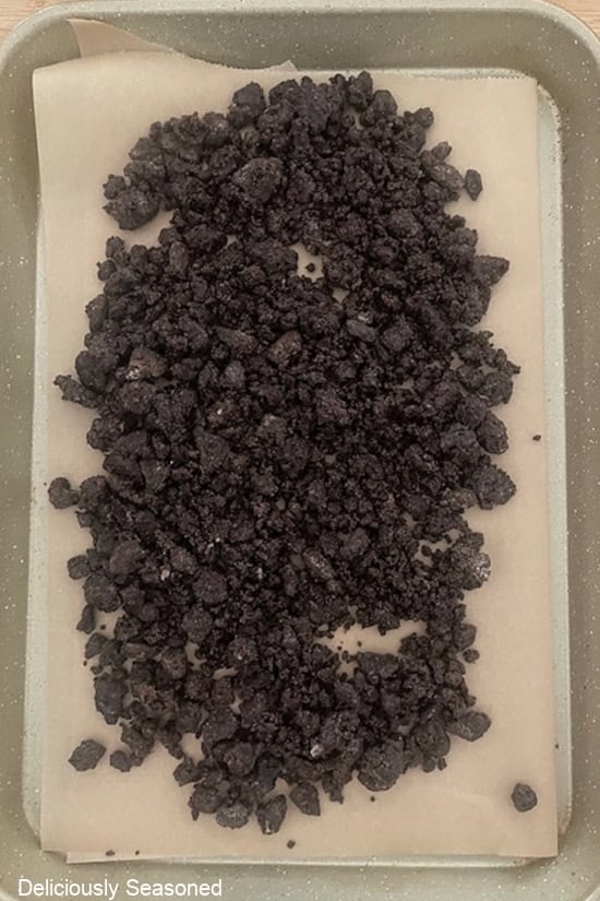 A baking sheet lined with parchment paper with chocolate Oreo crunch spread out on it getting ready to be baked in the oven.