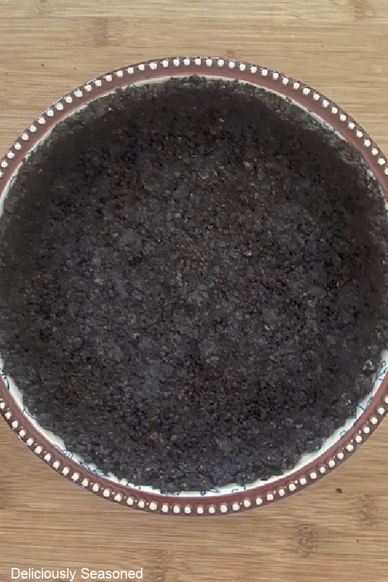 A wood surface with a blue pie dish with an Oreo cookie crust in it and up the sides of the dish.