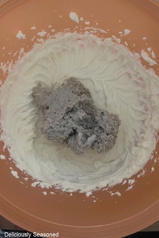 An orange mixing bowl with the beaten cream cheese mixture and the thick pudding mixture being mixed together.