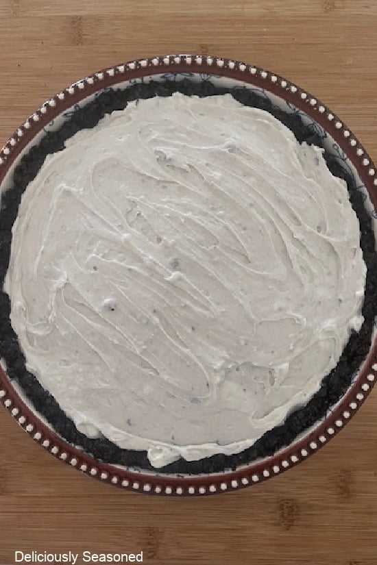 A wood surface with a blue floral pie dish with the pie filling added to the Oreo cookie crust.