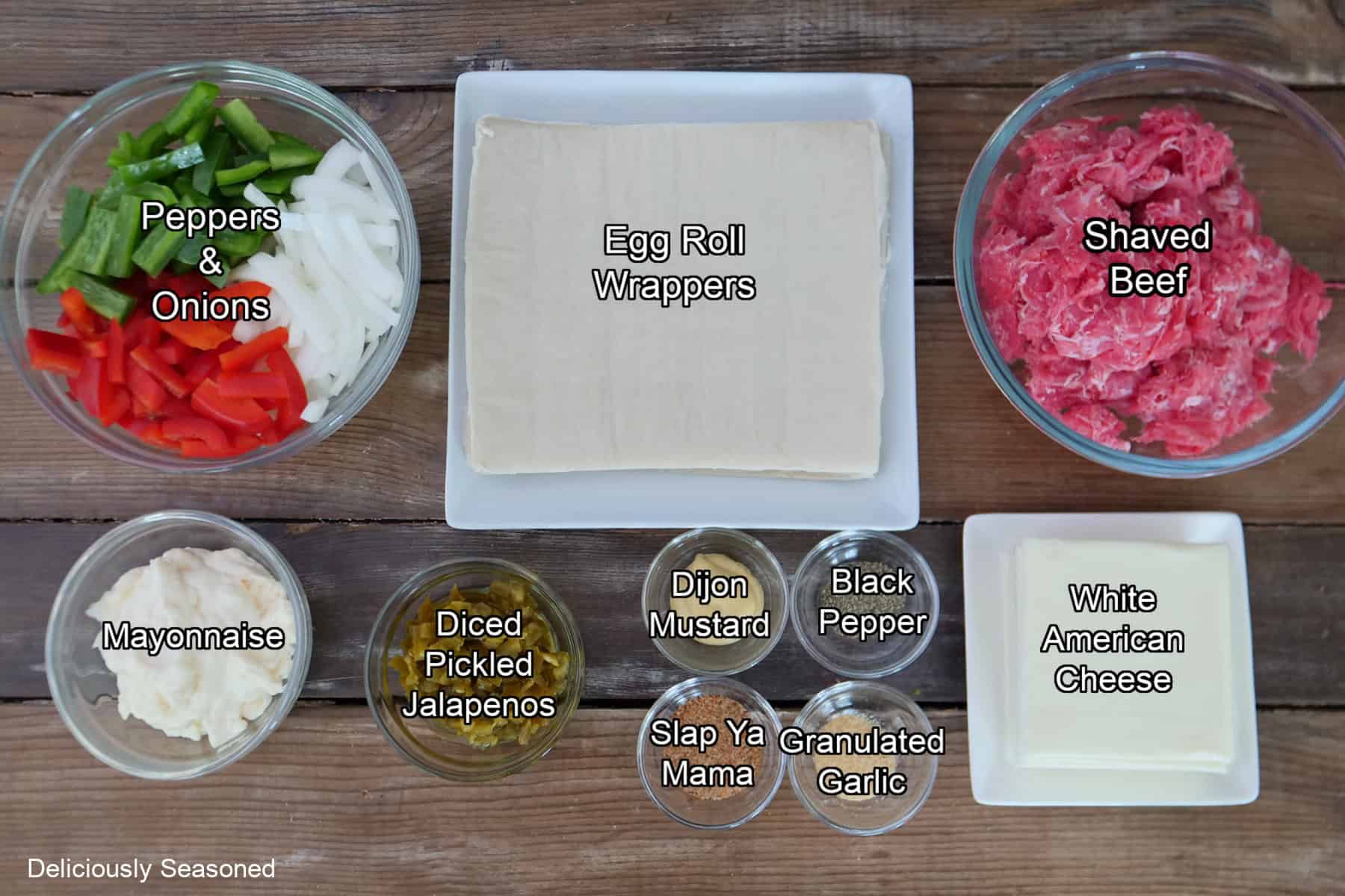 A wood surface with all the ingredients placed on it to make Philly cheesesteak egg rolls.