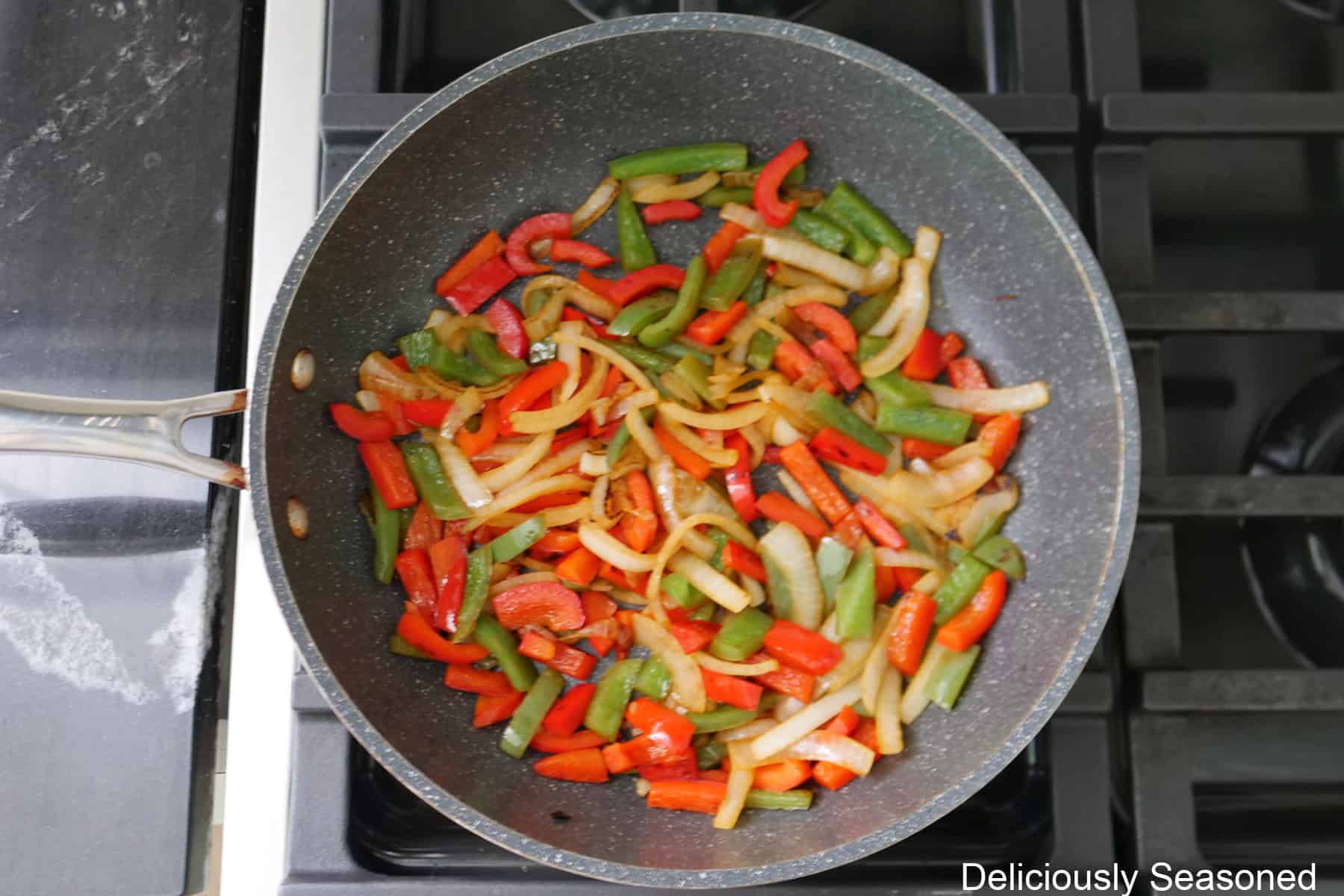 A frying pan with strips of red and green bell peppers and onions sautéing in the pan.