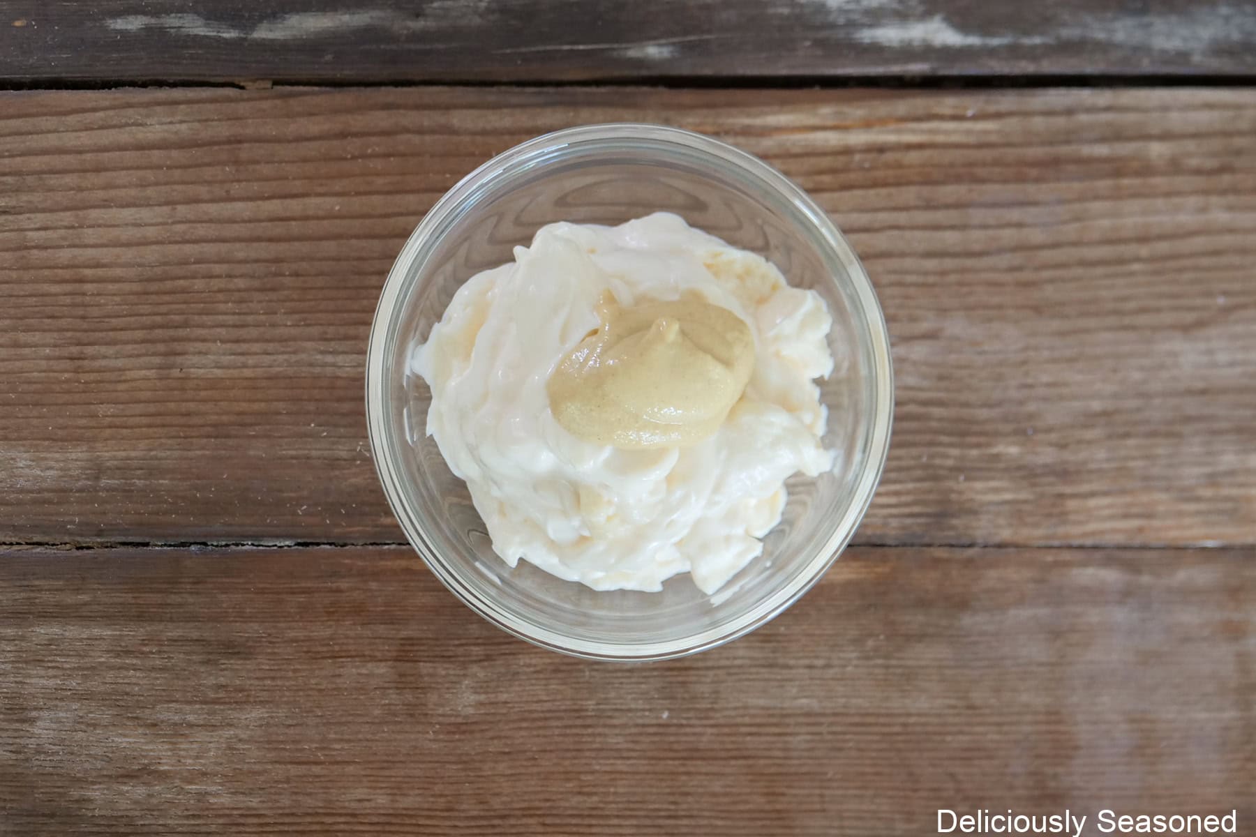 A wood surface with a small bowl filled with mayonnaise and Dijon mustard in it.