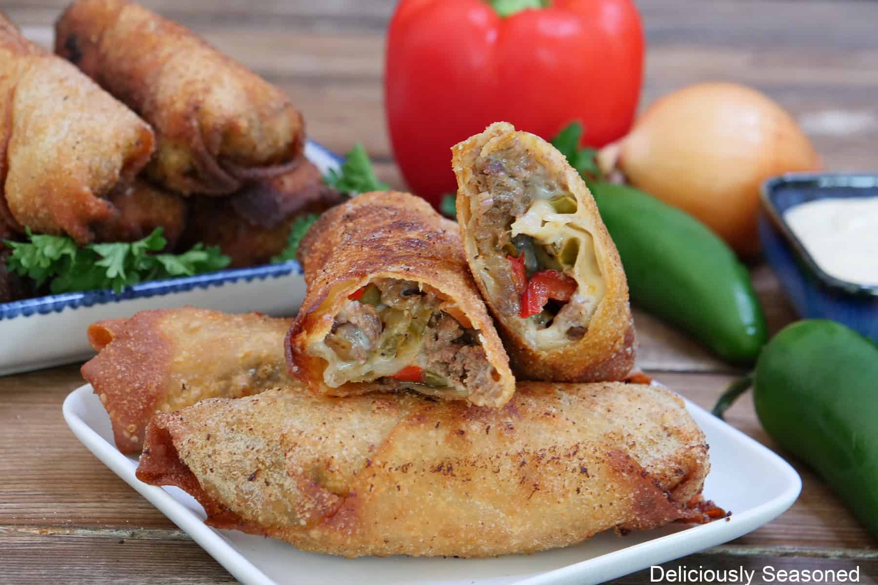 A wood surface with two white plates with deep fried egg rolls on them with one of them broke in half showing the inside ingredients.