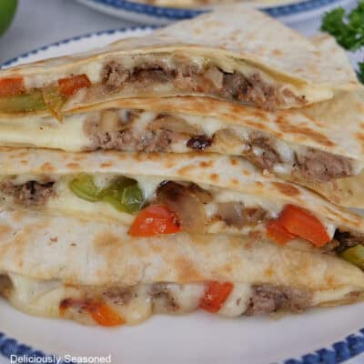 A white plate with blue trim with four pieces on Philly cheesesteak quesadillas stacked on top of each other.
