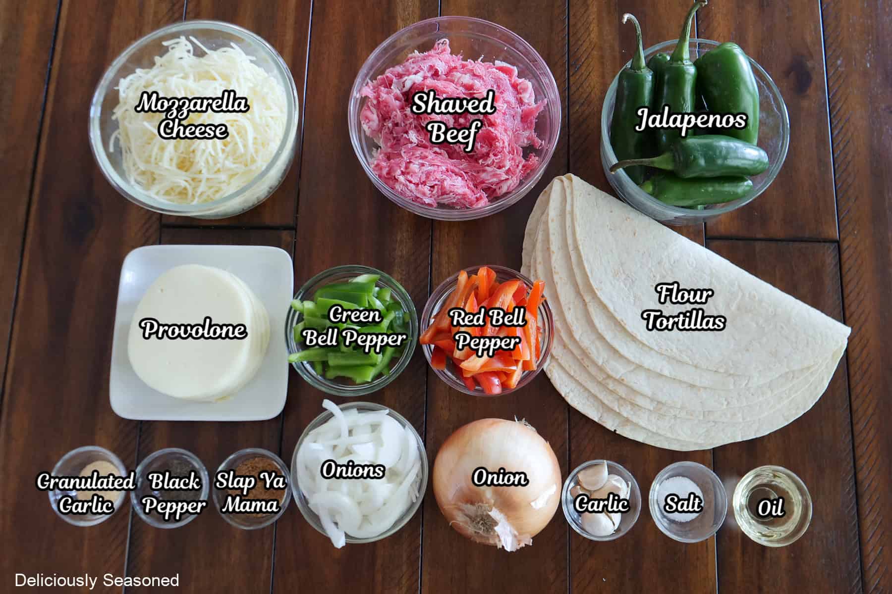 A wood surface with all the ingredients placed on it to make Philly Cheesesteak Quesadillas.