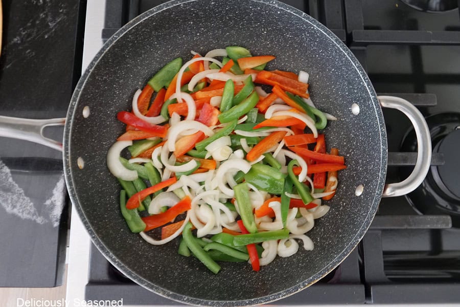 A frying pan with sauteed onions, and red and green bell peppers in it.