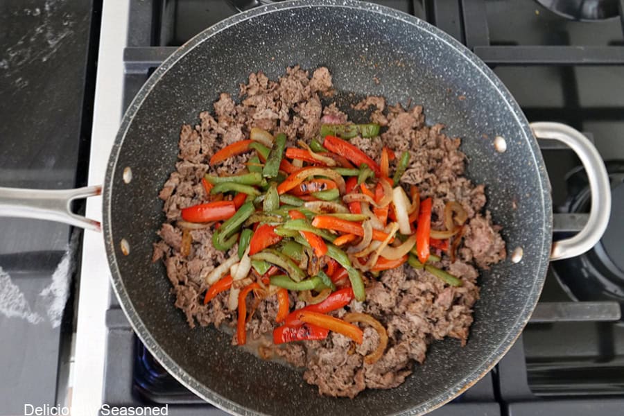 A frying pan with cooked beef, onions, and peppers in it.