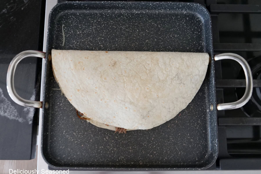 A frying pan with a Philly cheesesteak quesadilla in it before it is fried to golden.