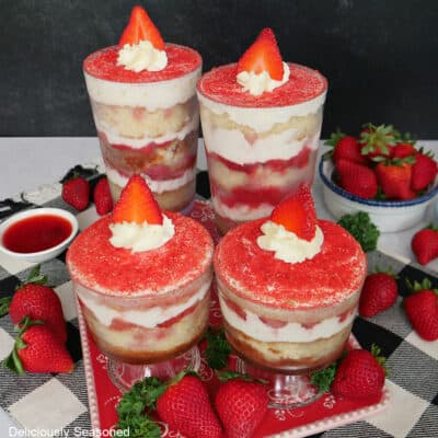 Four strawberry tiramisu parfaits on a black and white, and red surface.