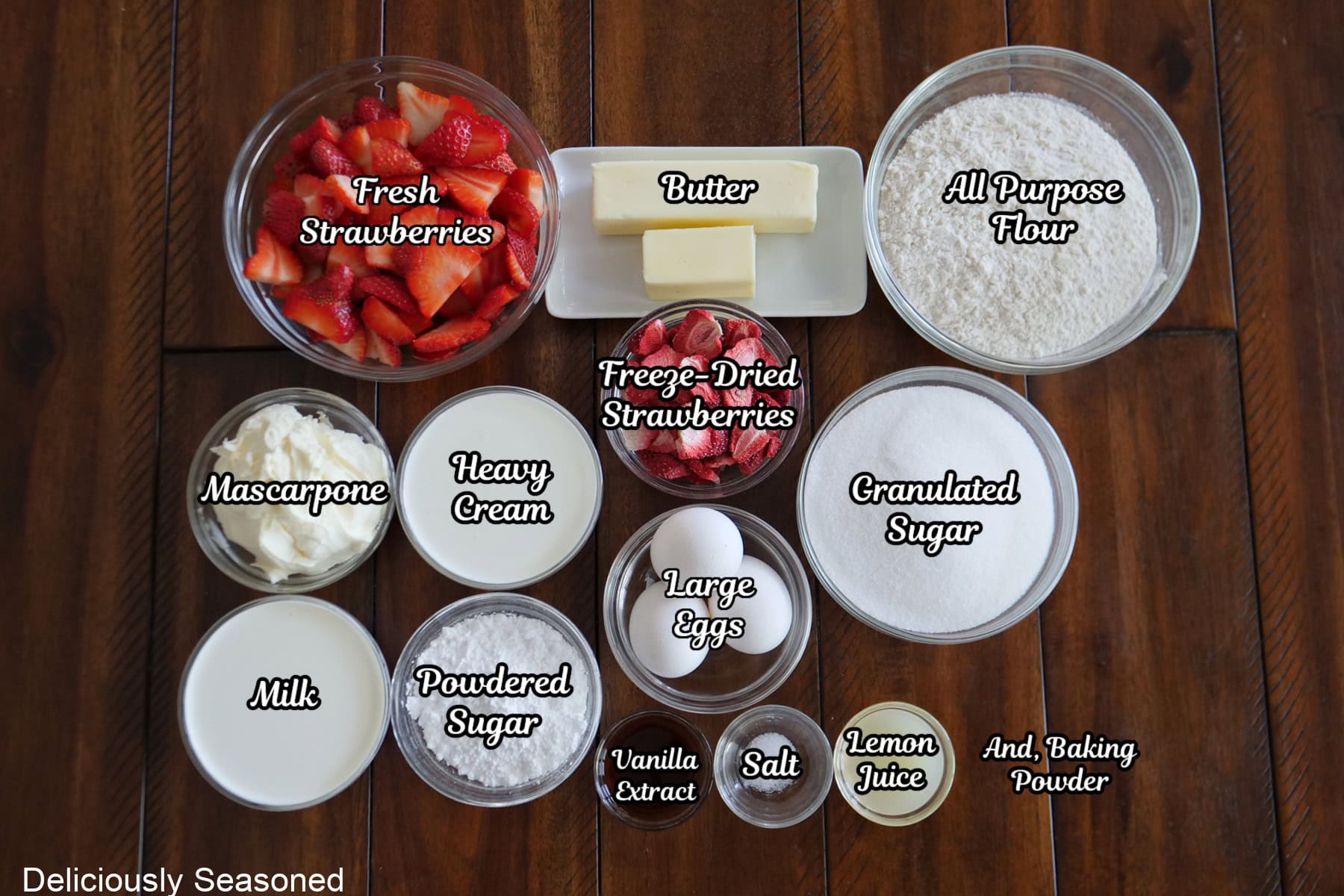 A wood surface of all the ingredients to make strawberry tiramisu parfaits placed on it.