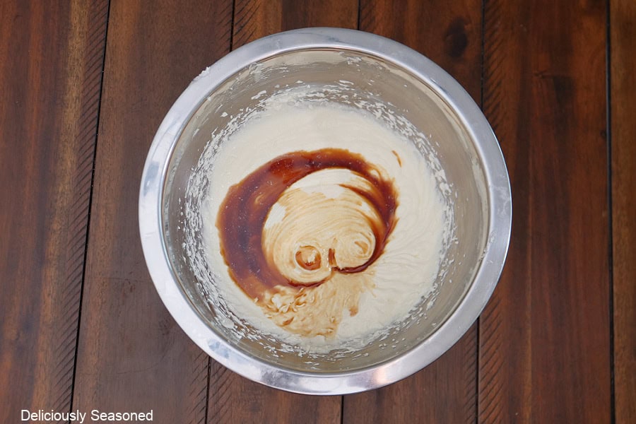 A wood surface with a metal mixing bowl with cake batter in it.
