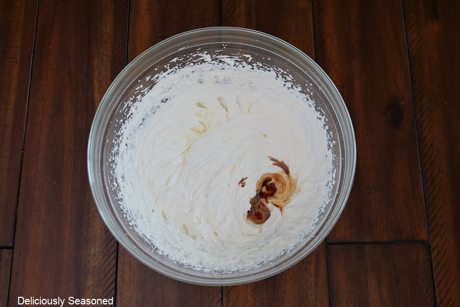 A glass mixing bowl with mascarpone whipped cream topping in it with vanilla poured into the bowl.
