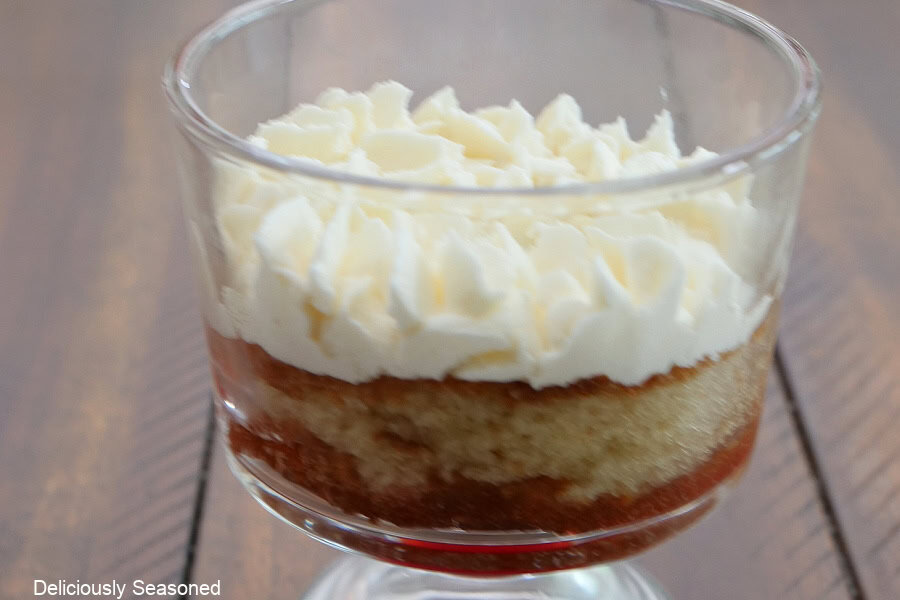 A parfait glass with a layer of strawberry filling, a layer of cake, another layer of strawberry filling and a layer of mascarpone whipped cream.