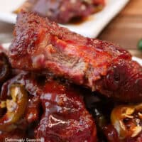 A wood surface with a white plate with a stack of smoked pork ribs on it with a bite taken out of the rib on top, and a title overlay at the top.