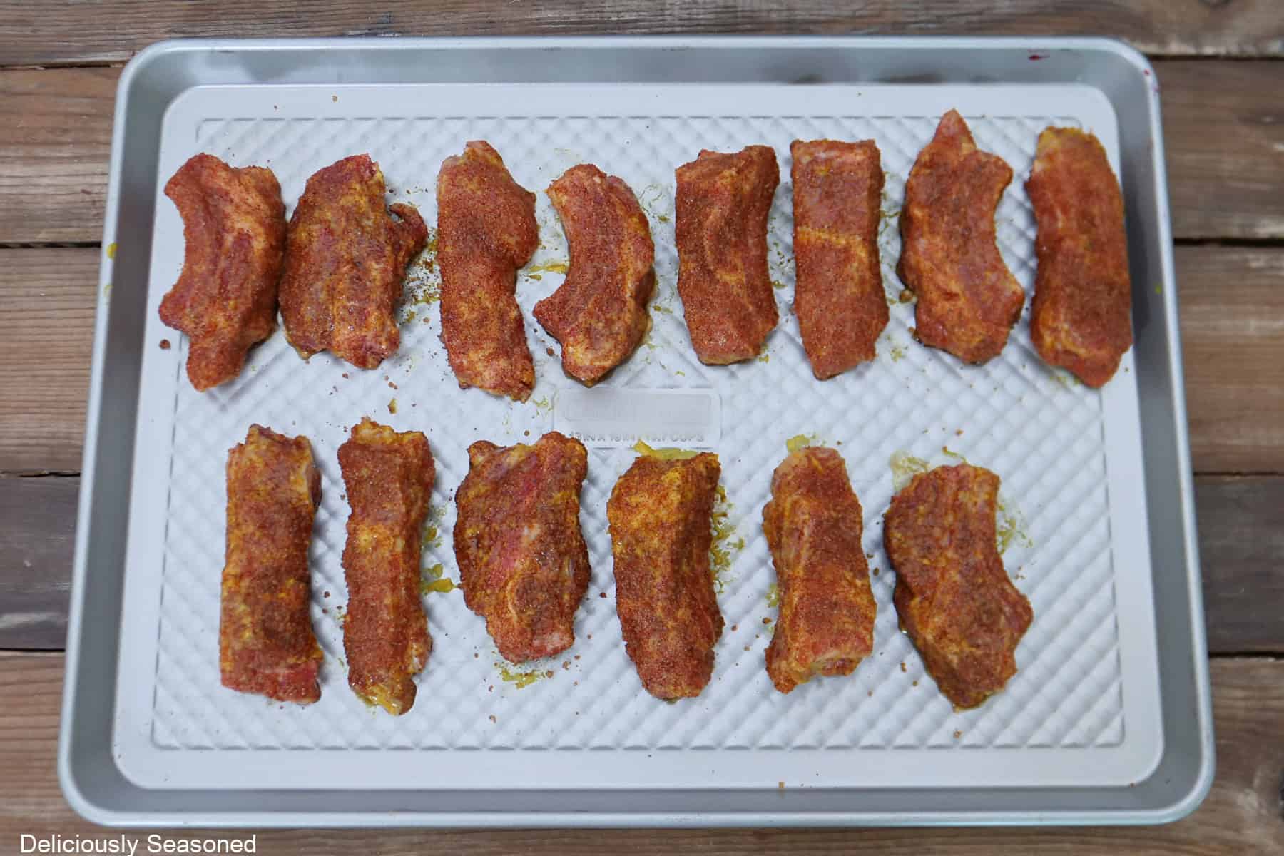 A silver baking sheet with heavily coated seasoned ribs on it.