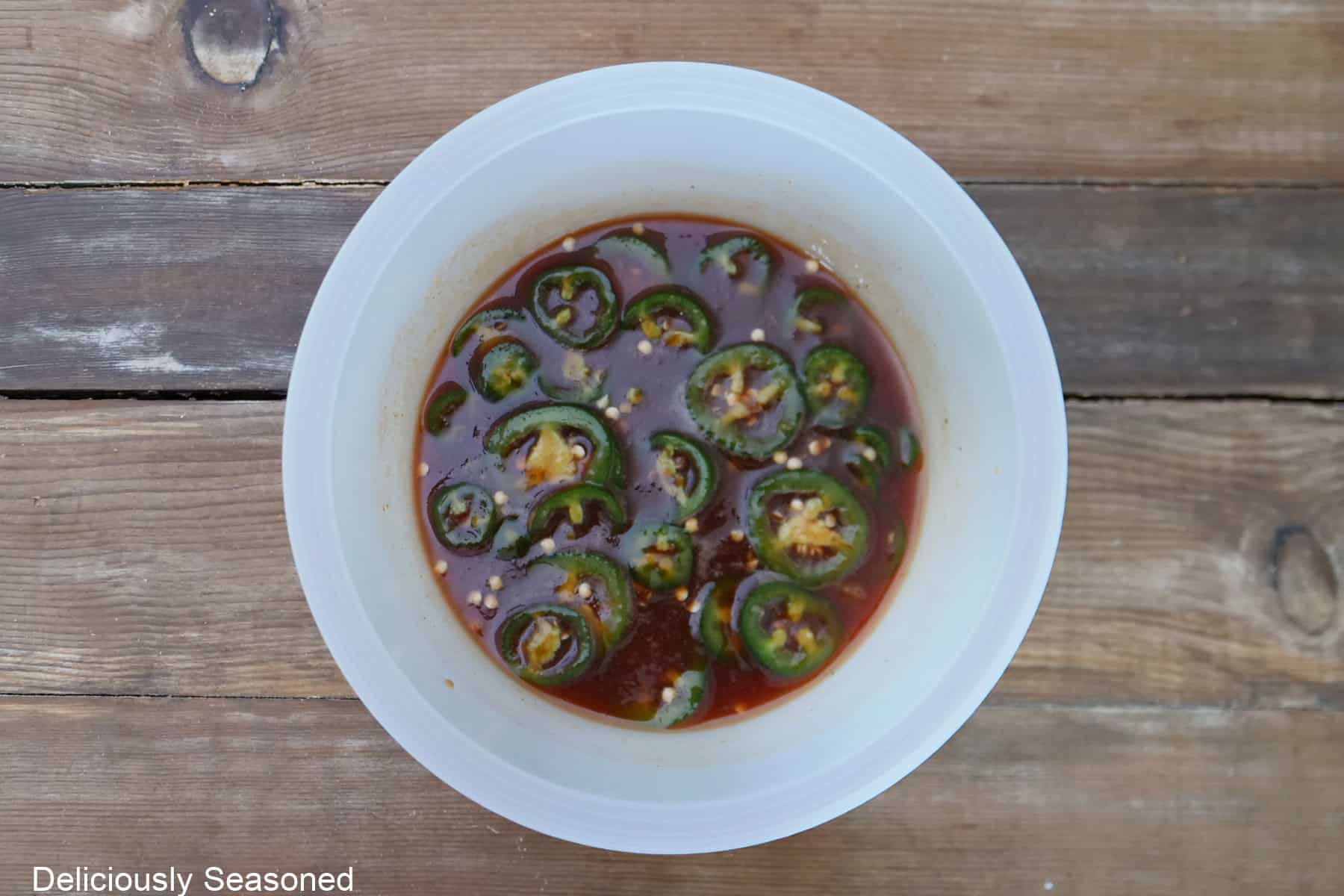 A wood surface with a white bowl filled with the sweet and spicy glaze ingredients in it.