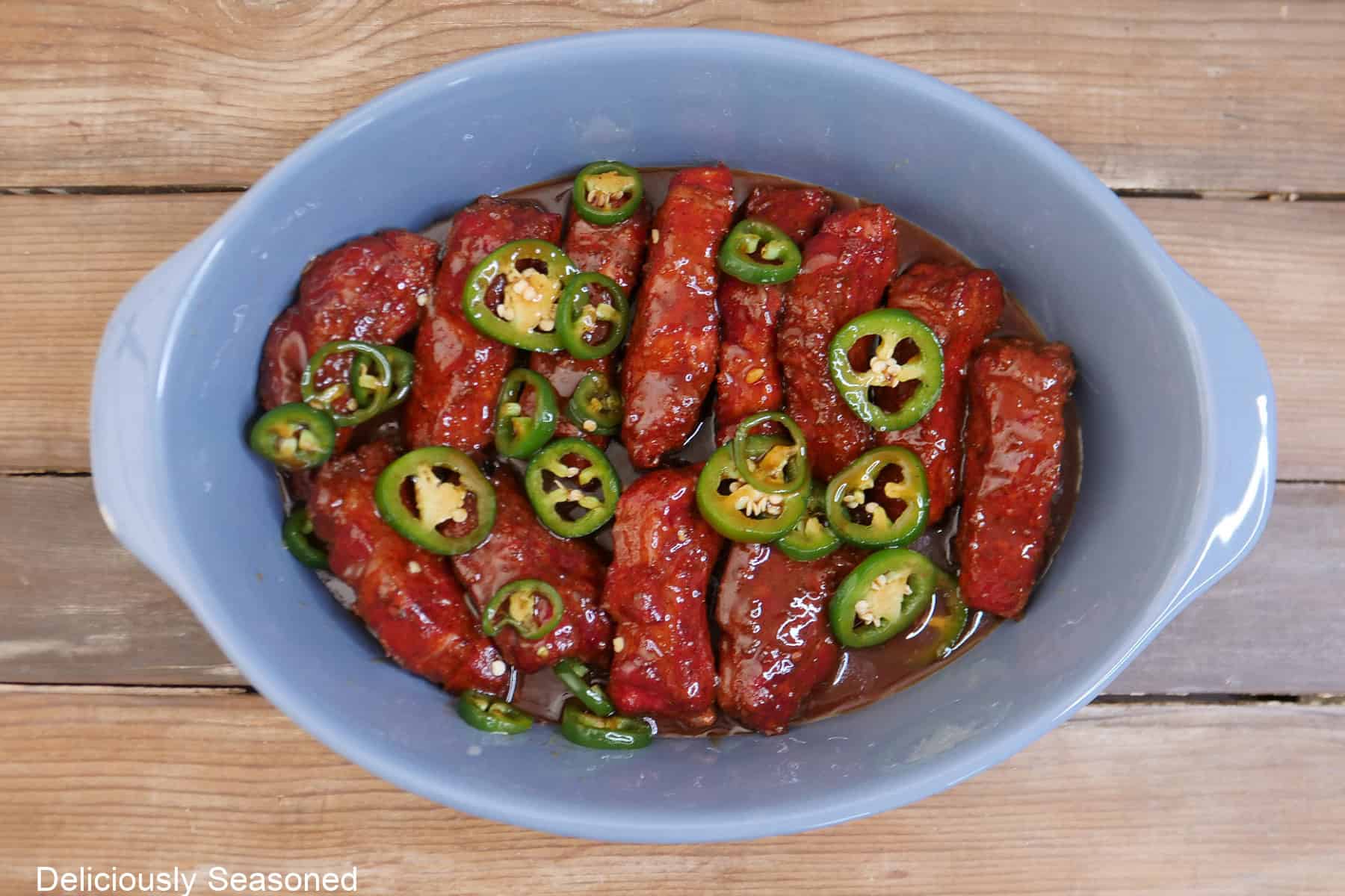 A light blue oval baking dish with smoked ribs and the sweet and spicy glaze ingredients in it.