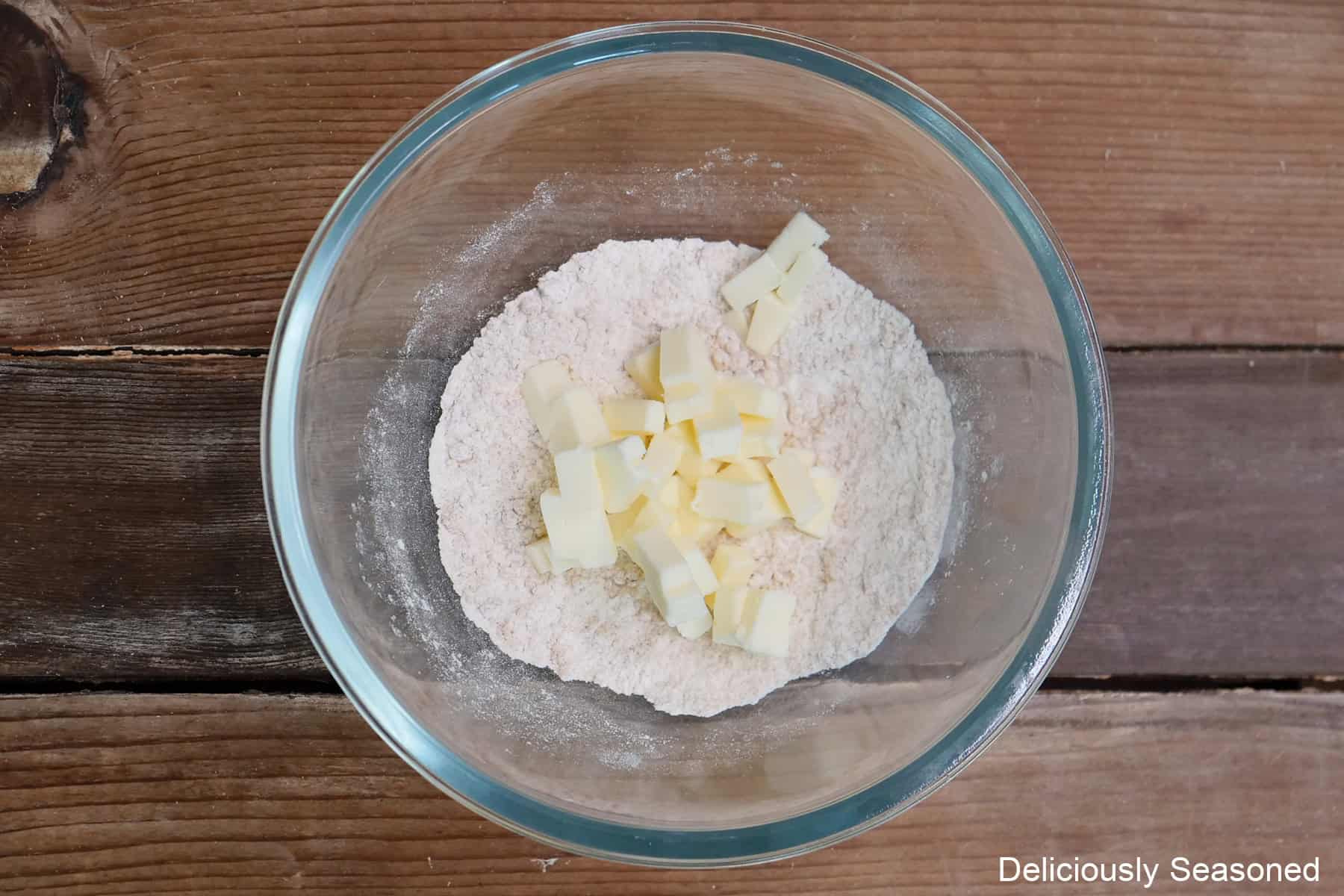 A wood surface with a glass bowl with flour, brown sugar, and butter in it.
