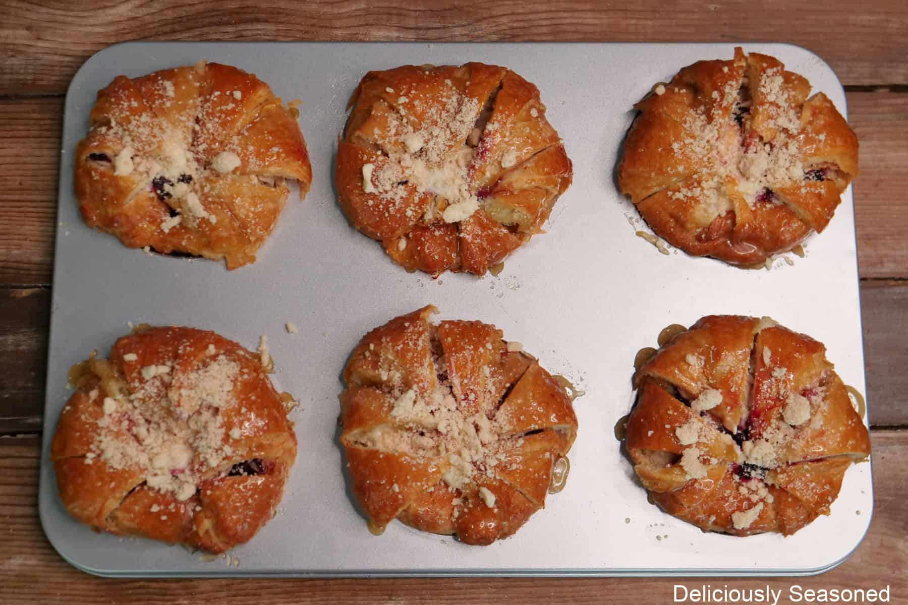 A silver baking sheet with six blackberry cream cheese croissants on it before being baked in the oven.