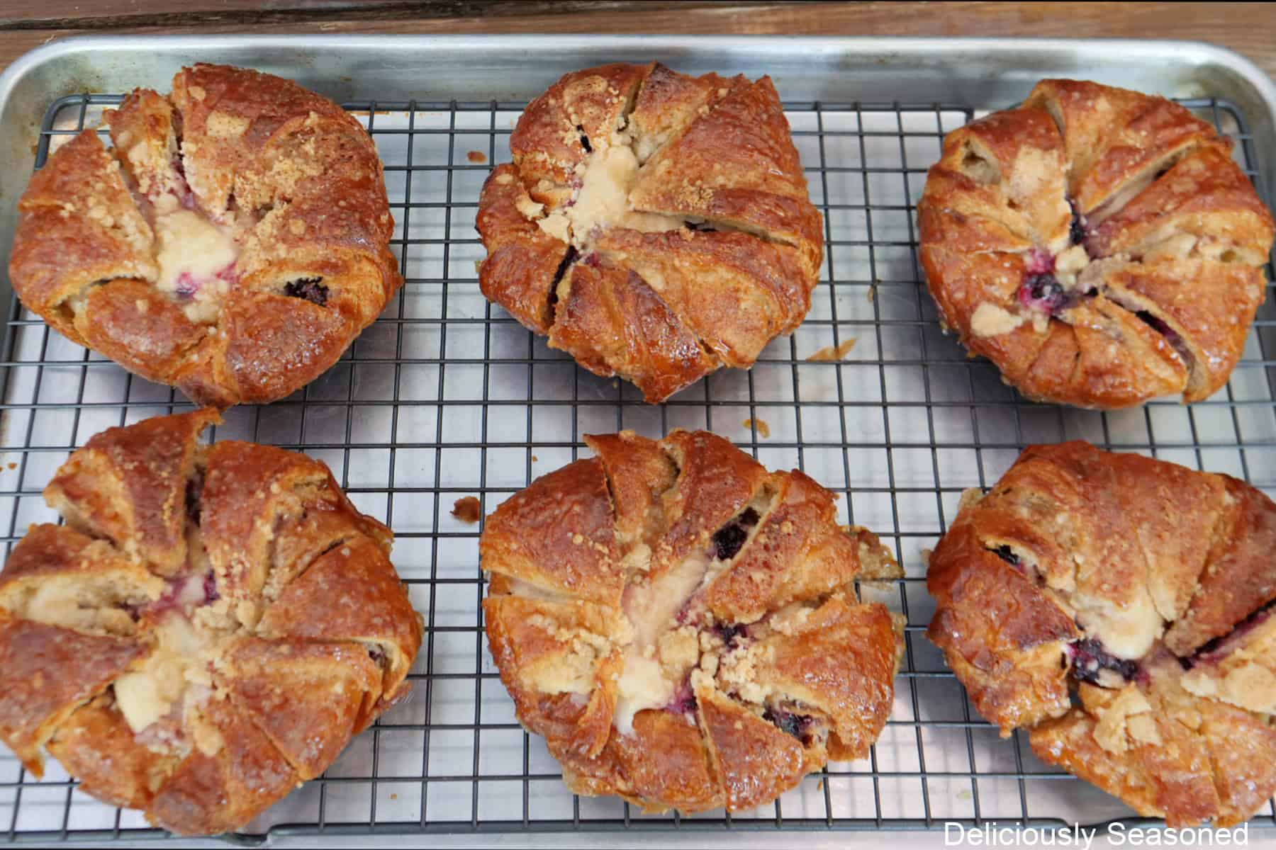 A baking sheet with a wire rack on it with six baked blackberry cream cheese croissants on it cooling.