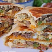 A white surface with a breakfast crunchwrap placed on it and has been cut in half and stacked on top of each other.