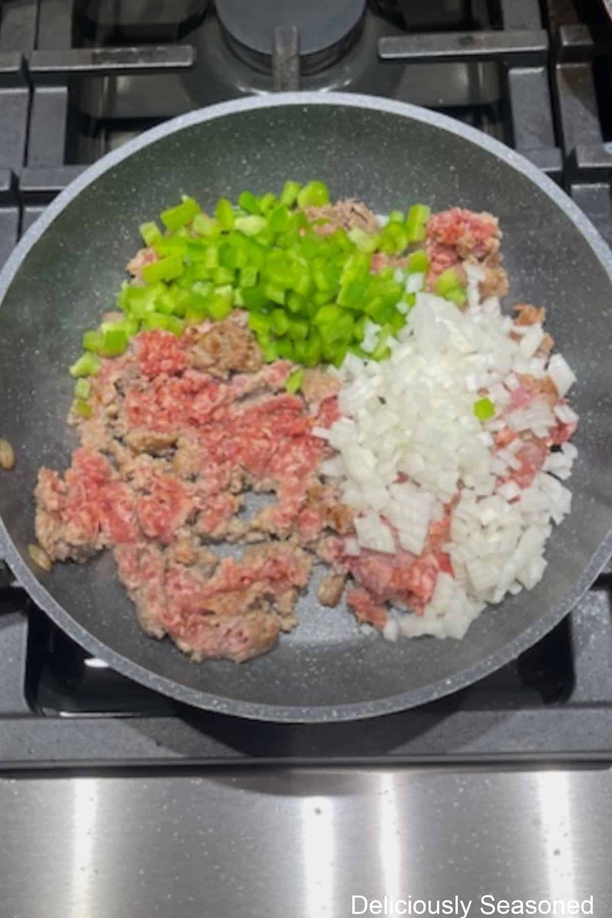 A frying pan with breakfast sausage, bell pepper, onions, seasoning in it.