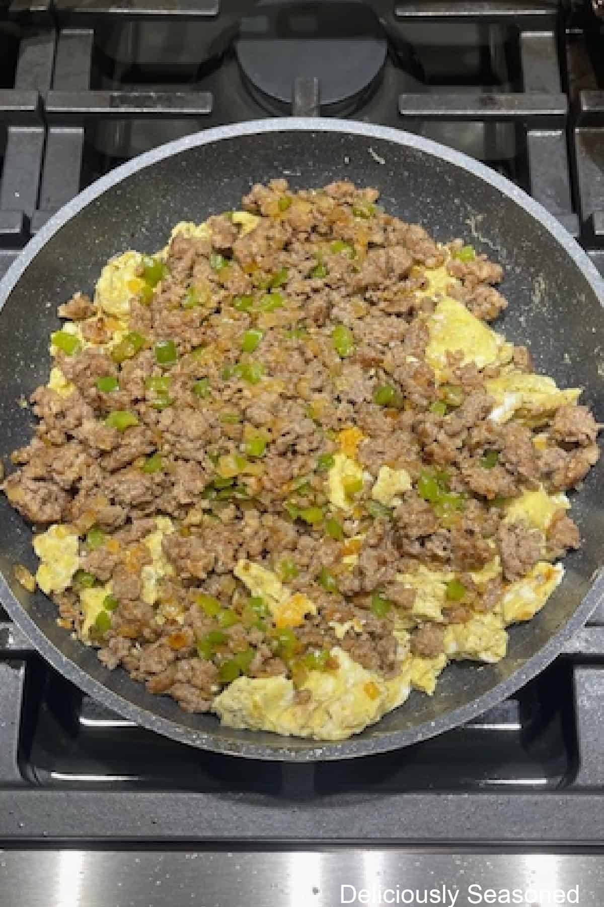 A frying pan with scrambled eggs with the sausage mixture added on top before being mixed together.
