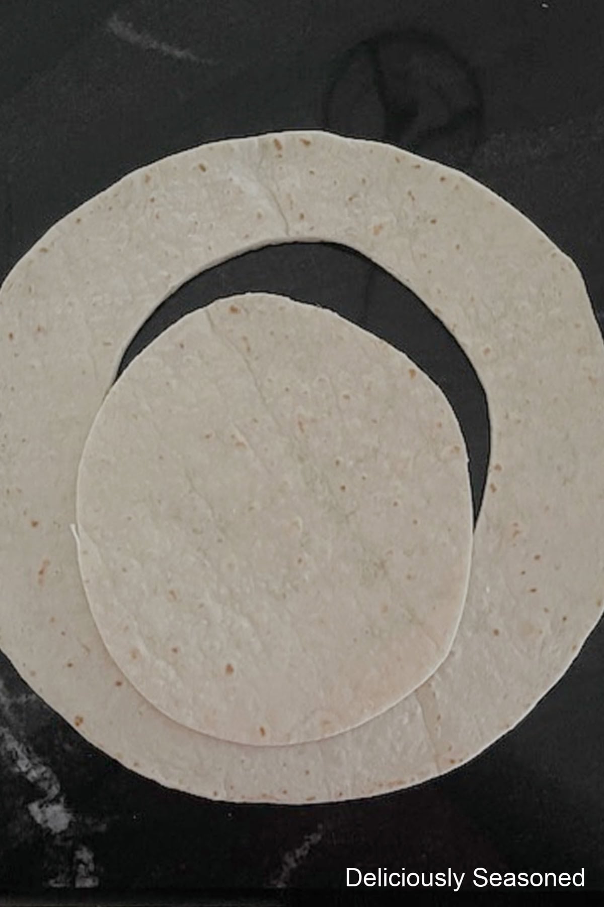 A black countertop with a flour tortilla on it with a piece of the tortilla in the center cut out.