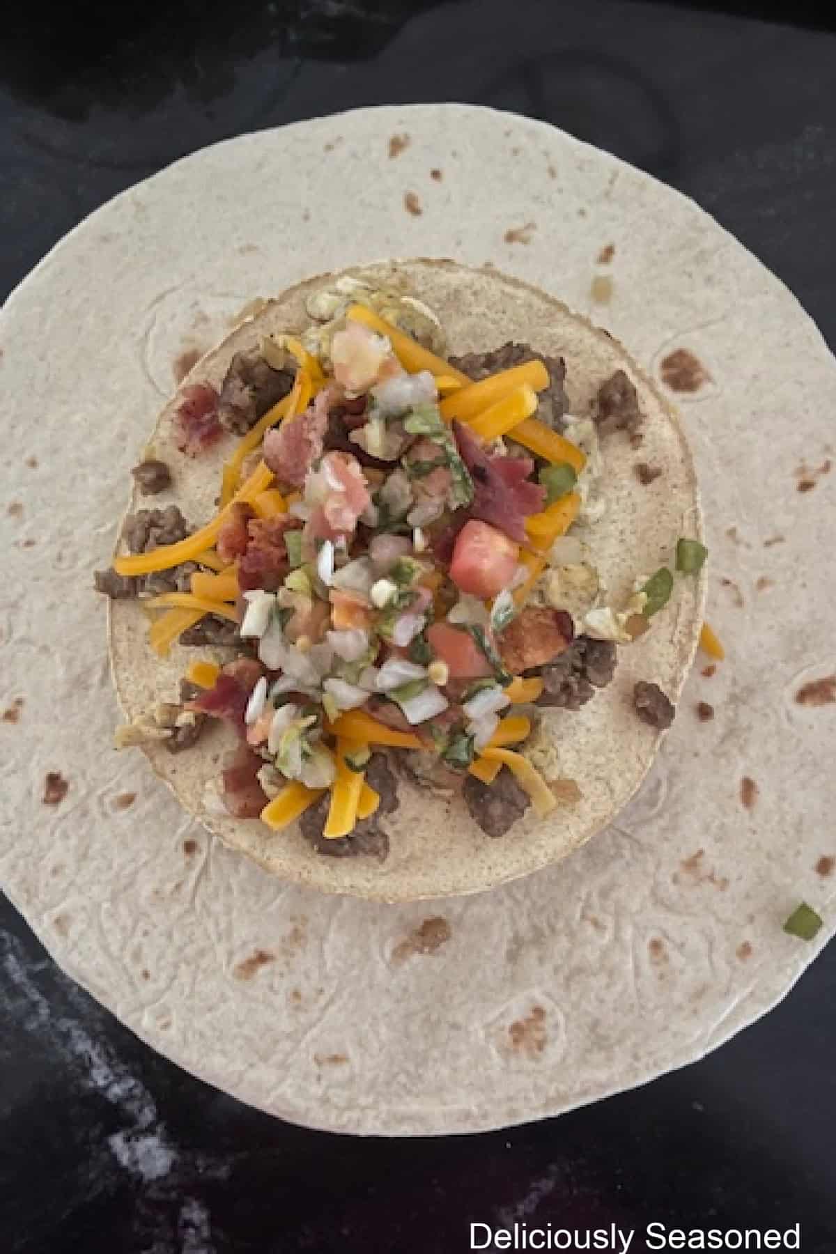 A flour tortilla with the breakfast crunchwrap ingredients on it before being wrapped up.