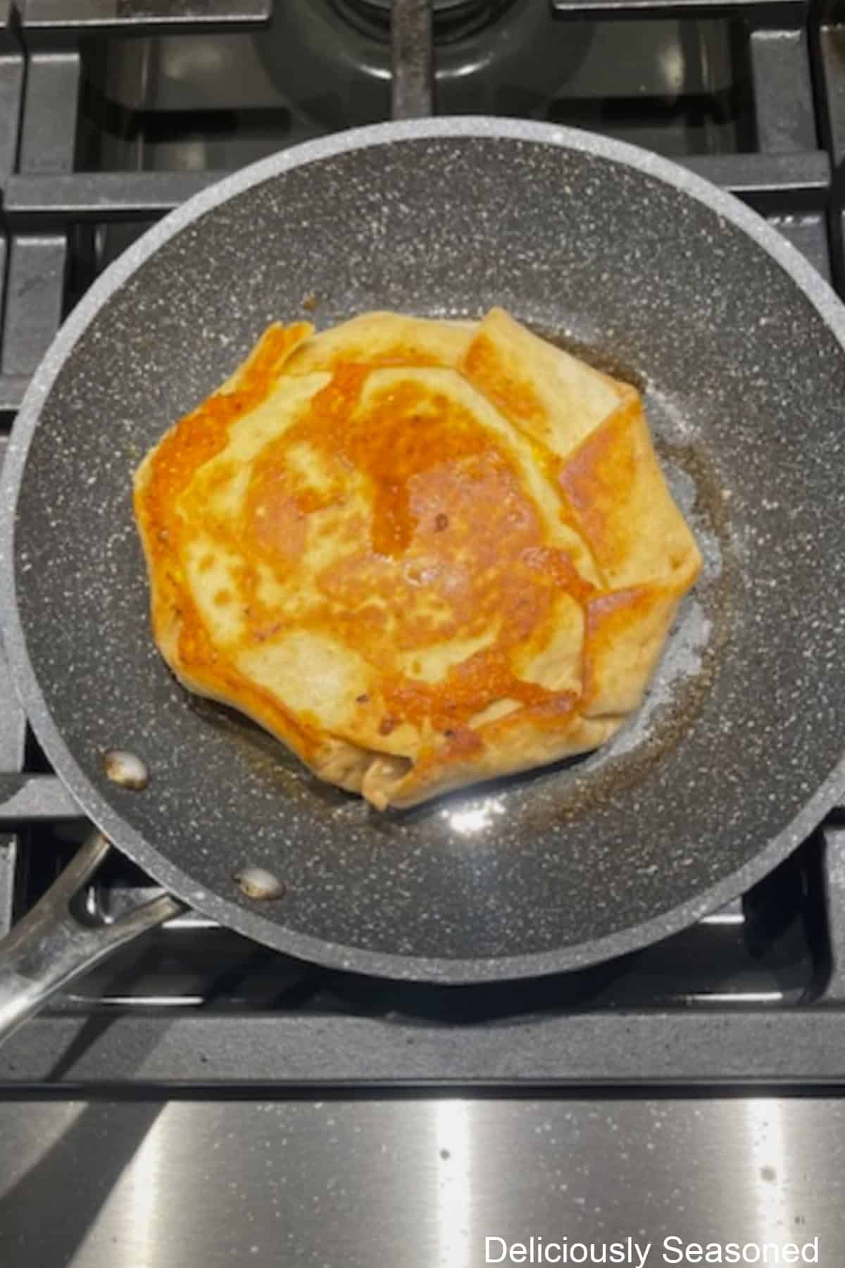 A frying pan with melted butter and a crunchwrap being fried in it.