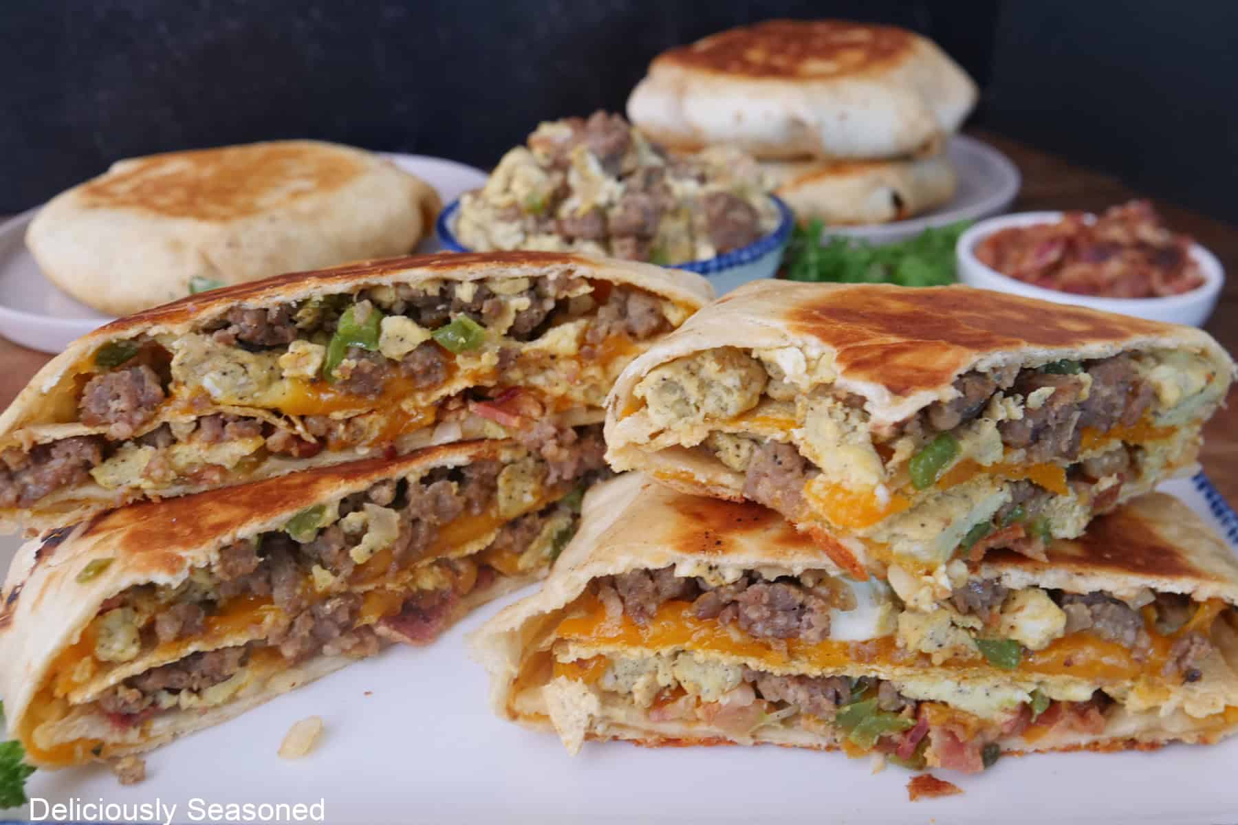 A white surface with five breakfast crunchwraps on it with two of them cut in half and stacked on top of each other showing the inside ingredients.