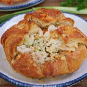 A round white plate with blue trim with a round store-bought croissant on it filled with a savory rotisserie chicken mixture.