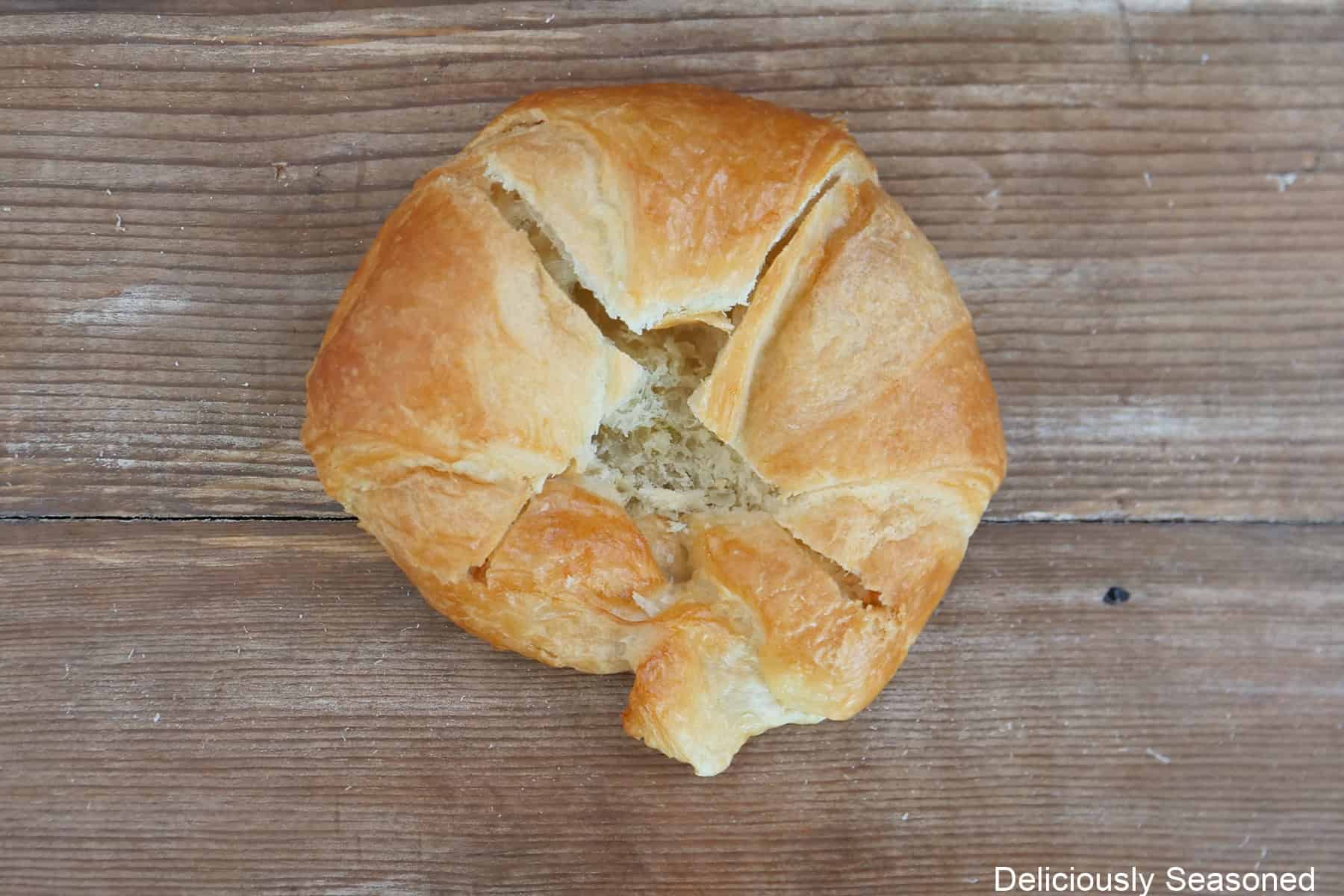 A wood surface with a round store-bought croissant on it that has been cut with an X across the top.