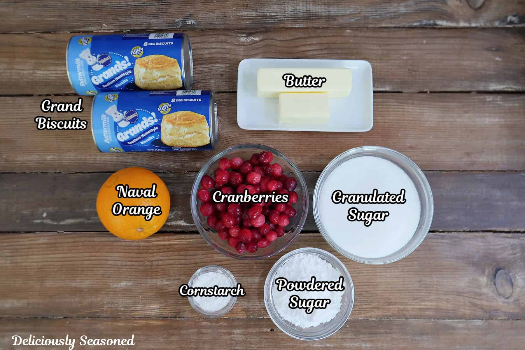 A rustic wood surface with all the ingredients placed on it to make cranberry orange monkey bread.