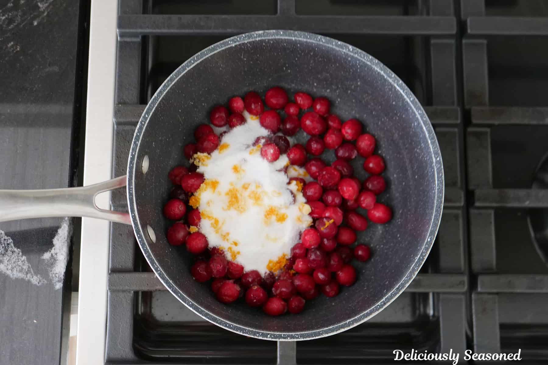 A saucepan with cranberries, sugar, orange zest, and cornstarch in it before being mixed together.