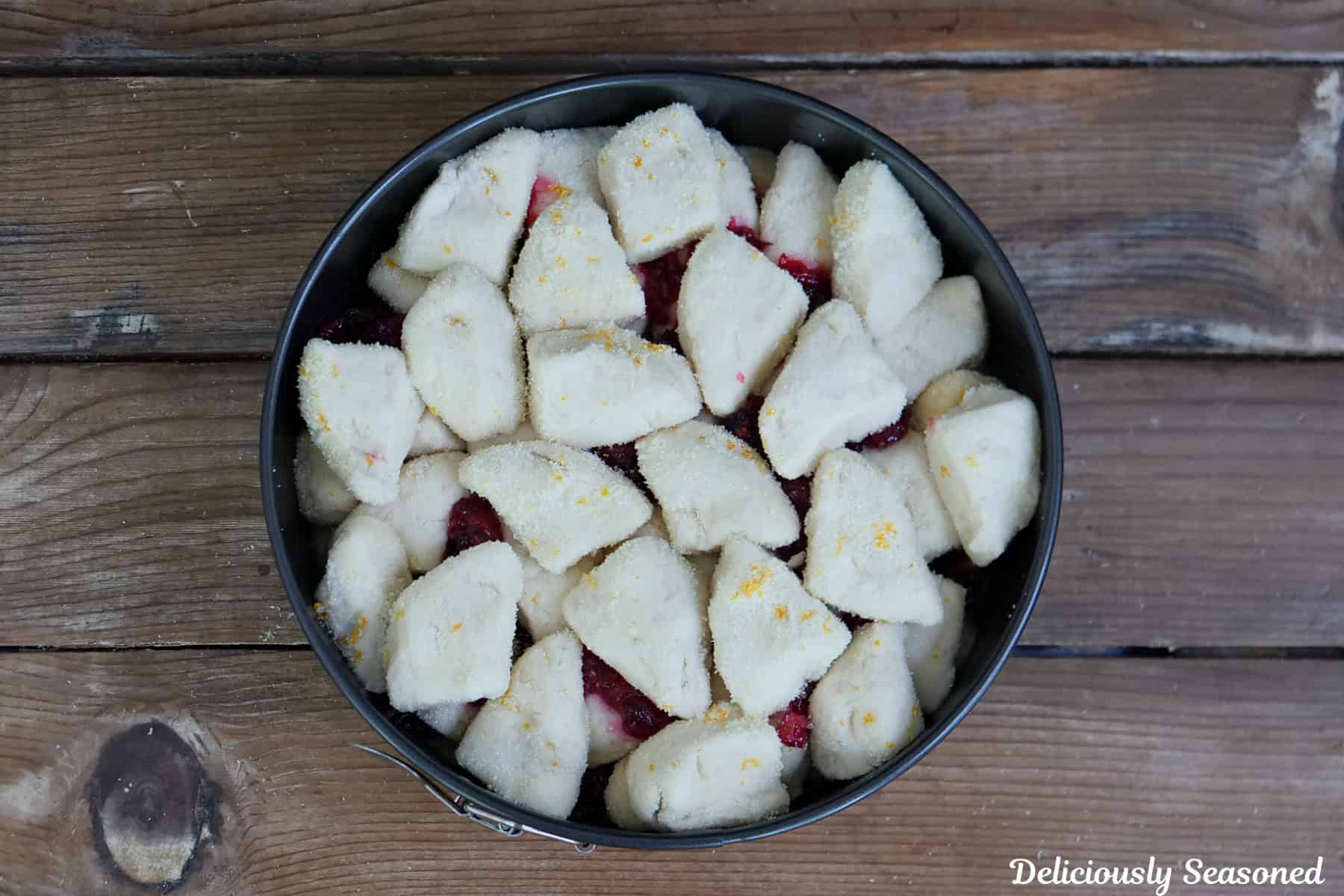 A rustic wood surface with biscuit pieces on top of the cranberry orange filling.