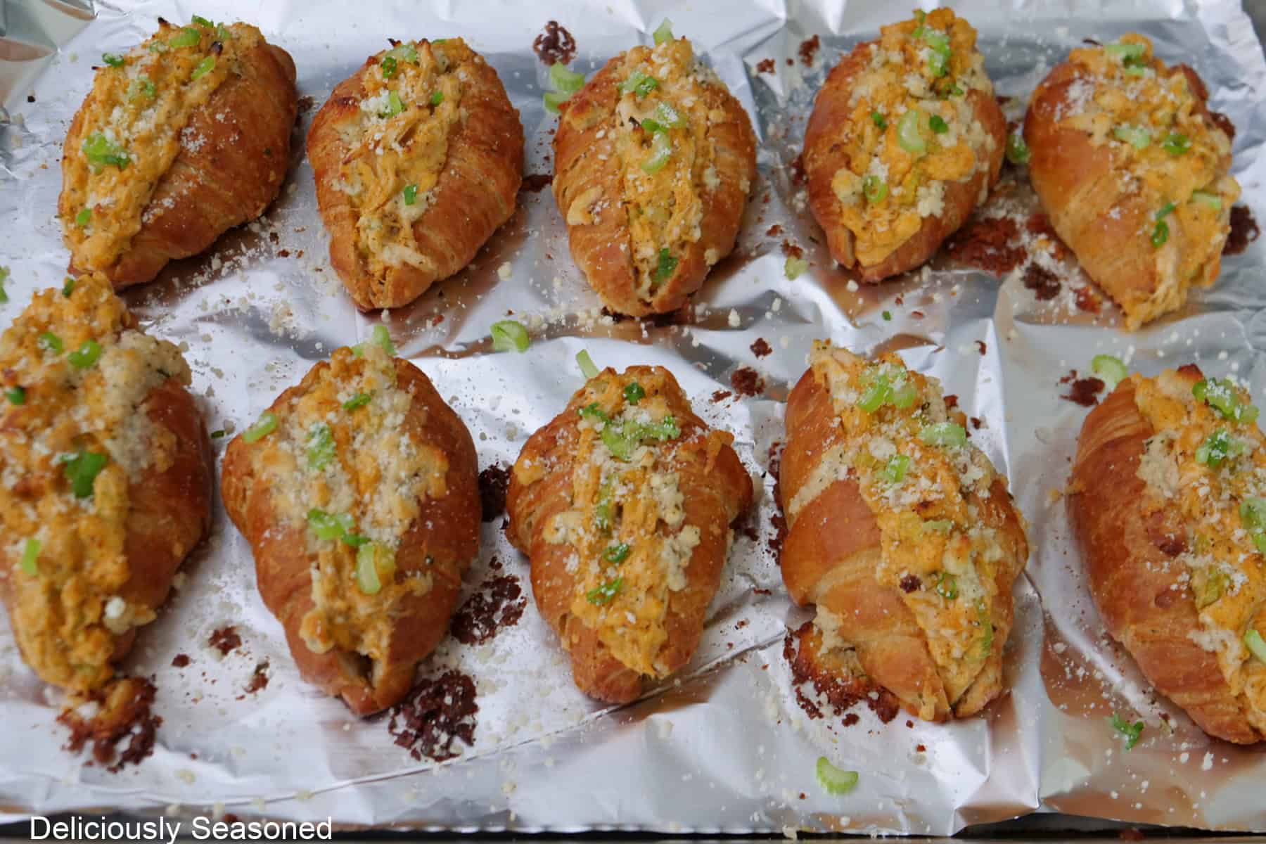 A foil lined baking sheet with ten baked mini buffalo chicken croissants placed on it.