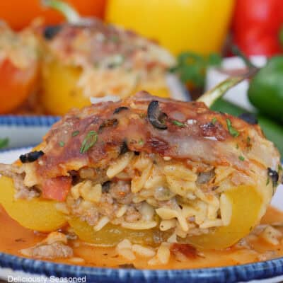 A white plate with blue trim with a yellow pepperoni pizza stuffed pepper on it with more peppers in the background.