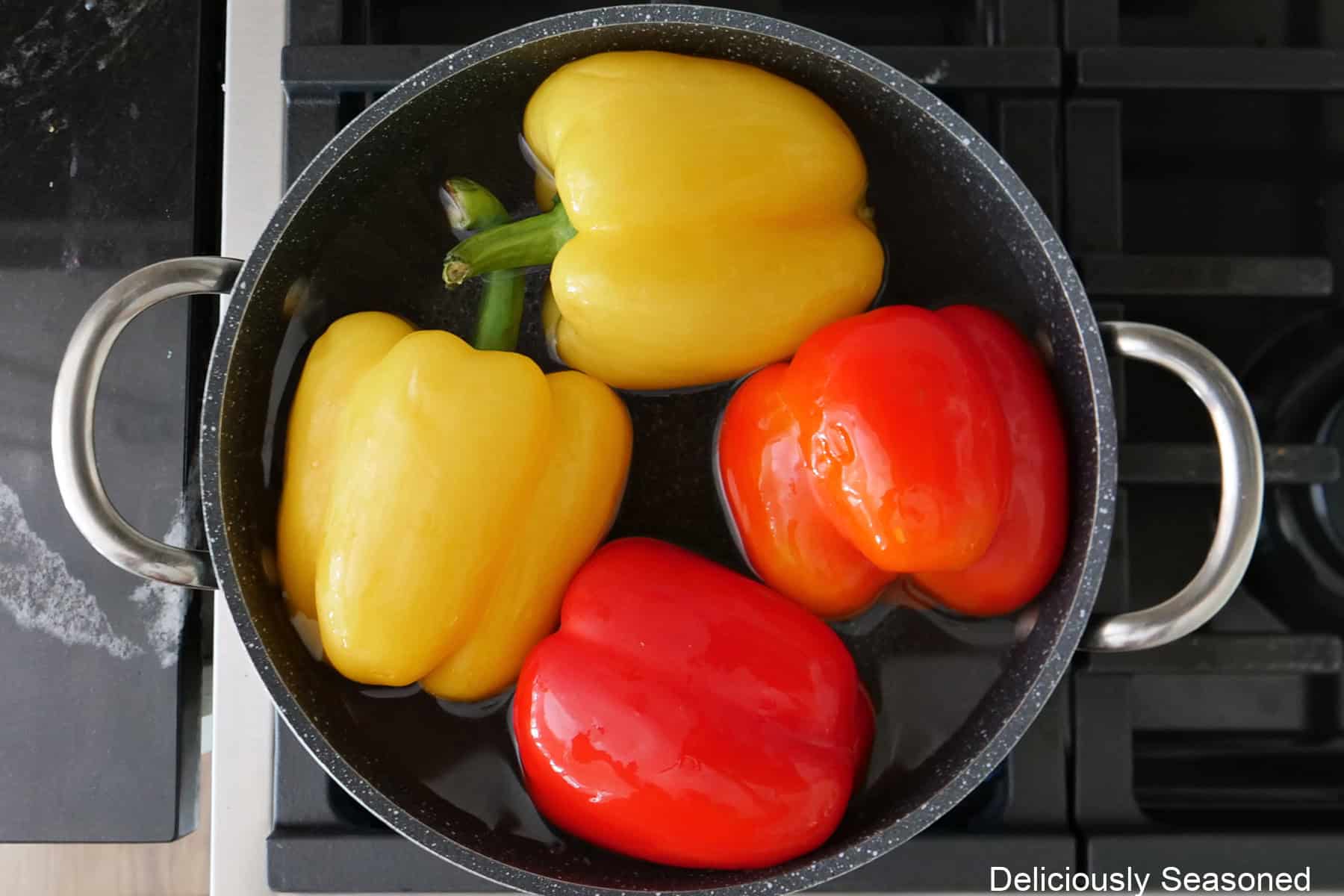 A saucepan with four bell peppers, two red and two yellow, in it.