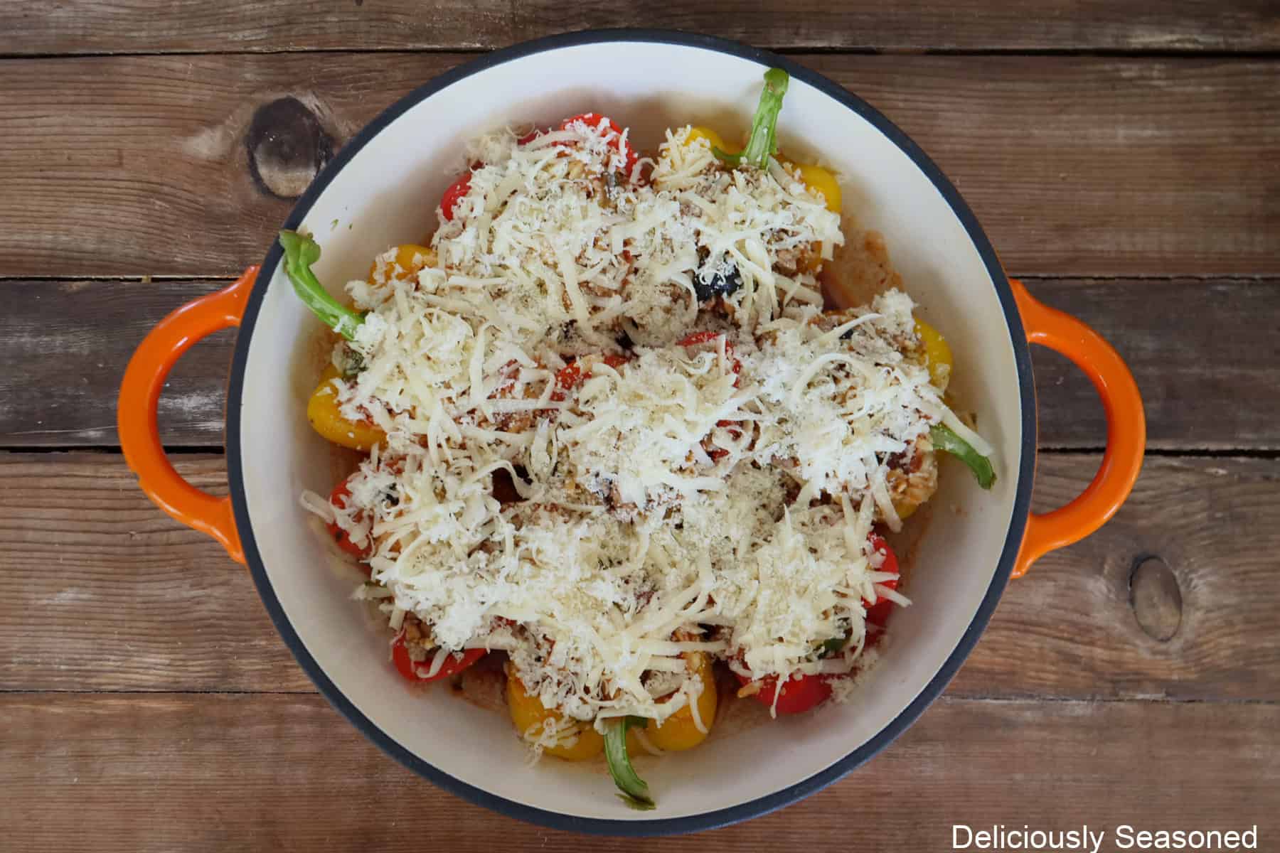 A cast iron skillet with eight bell pepper halves stuffed with pepperoni pizza ingredients and topped with shredded mozzarella cheese before being baked in the oven.