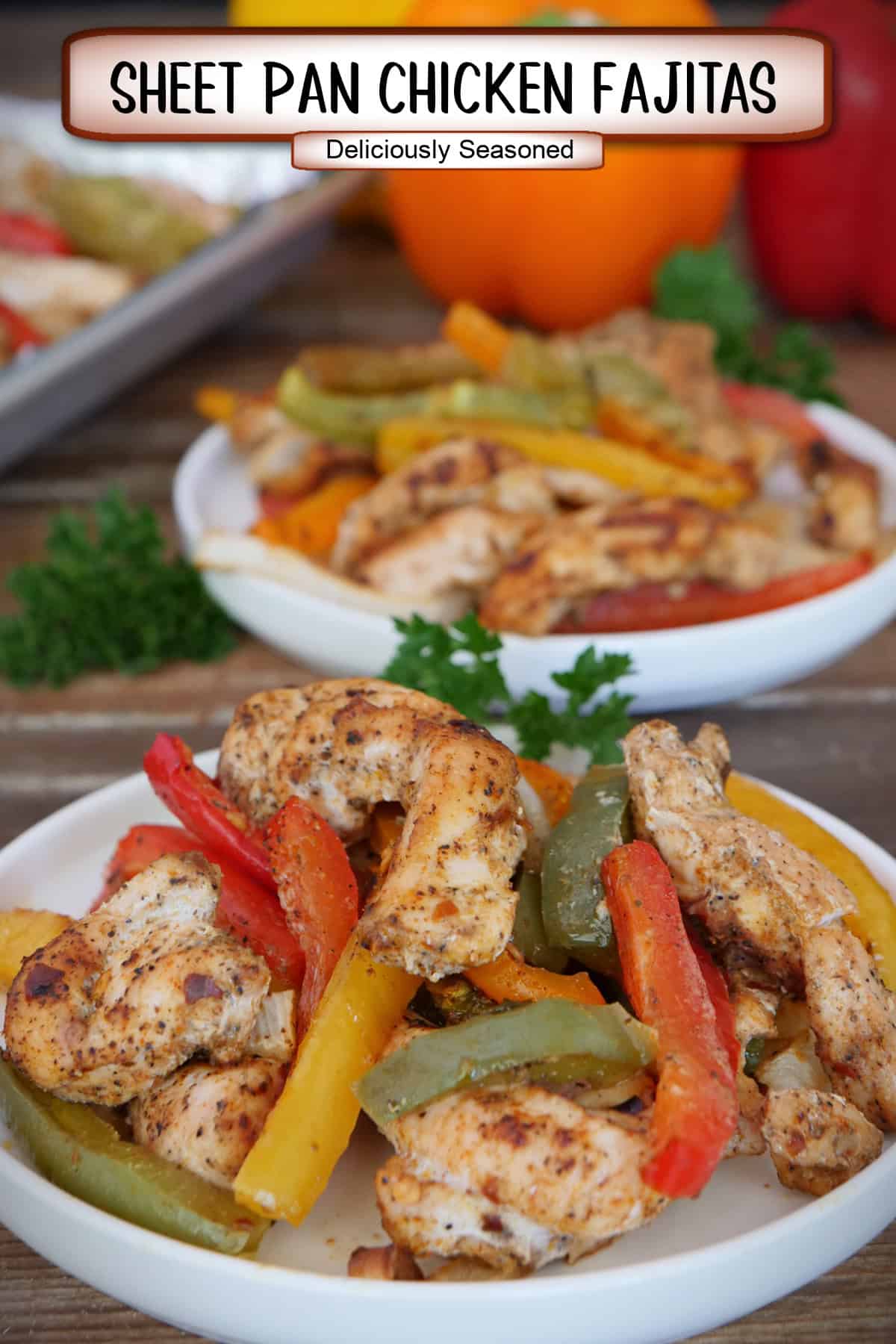 A wood surface with two white bowls filled with sheet pan chicken fajitas with an orange and red bell pepper in the background, and a title overlay at the top.