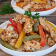 A wood surface with a white round plate filled with chicken fajitas.