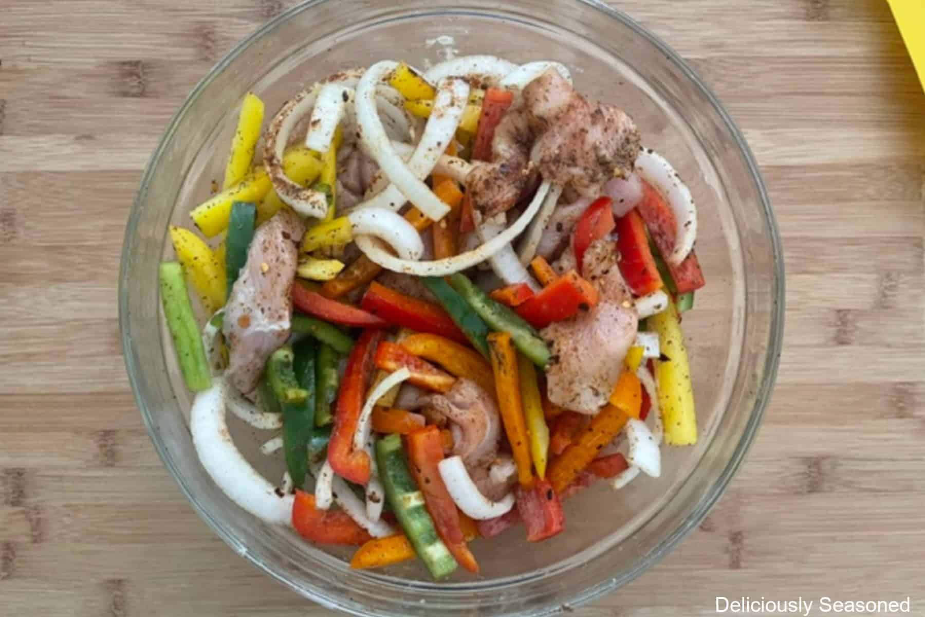 A wood surface with a glass bowl filled with all the chicken fajitas ingredients in it.