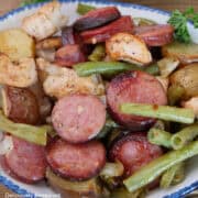 A serving of sheet pan chicken and sausage in a white bowl with blue trim.