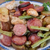 A serving of sheet pan chicken and sausage in a white bowl with blue trim.